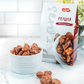 Crispy praline pecans in white ridged bowl with Watanut package, scattered nuts on marble surface