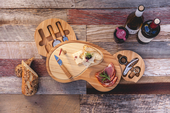 Bamboo golf-club-shaped cheese board featuring two connected cutting surfaces with cheese, charcuterie, stainless steel serving tools, and wine bottle.