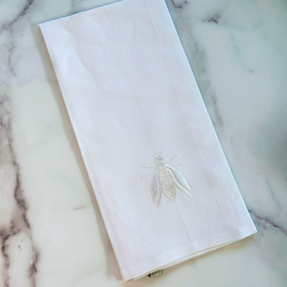 White linen kitchen towel with embroidered wheat motif, laid flat on marble
