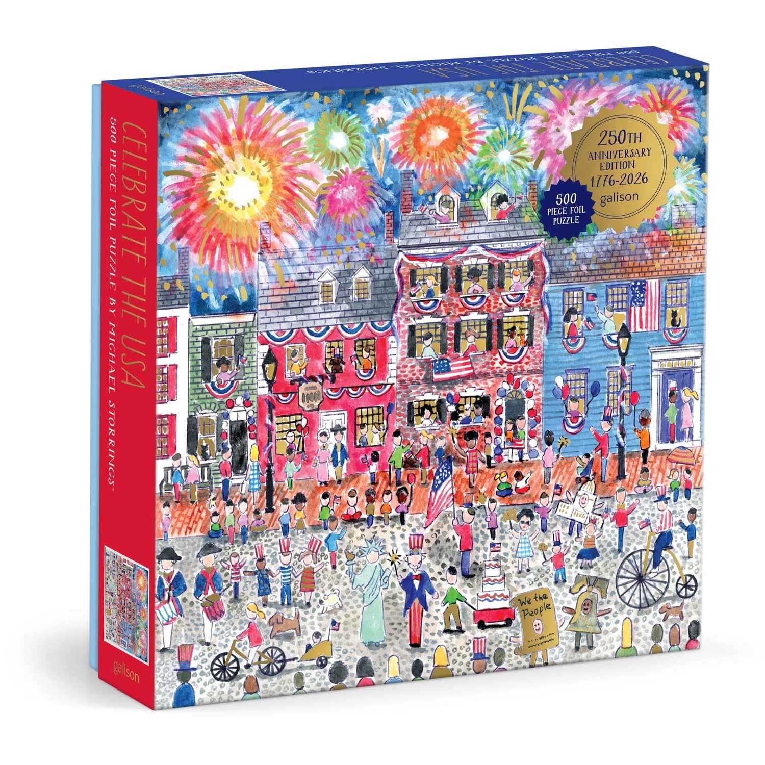 Celebrate the USA 500-piece foil puzzle box featuring Michael Storrings' patriotic illustration of a bustling boardwalk scene with colorful fireworks, festive crowds, and red brick buildings decorated for Independence Day
