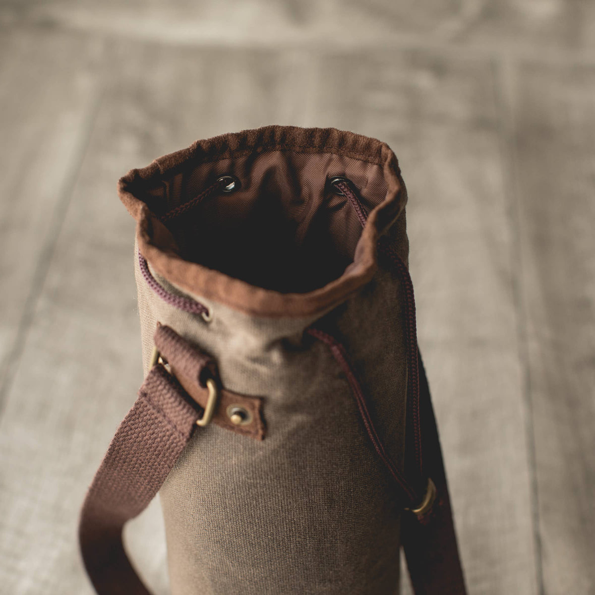 Distressed waxed canvas wine tote bag in tan with brown leather shoulder strap and gold-tone hardware, open top showing insulated interior lining.