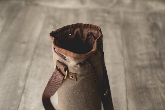 Distressed waxed canvas wine tote bag in tan with brown leather shoulder strap and gold-tone hardware, open top showing insulated interior lining.