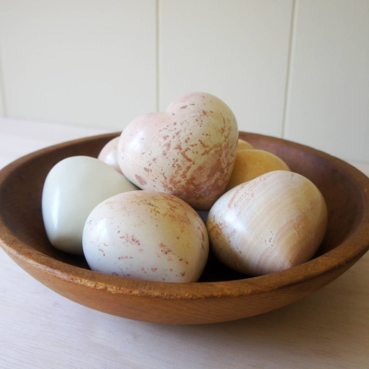 Polished soapstone hearts in cream, pink, and rust tones nestled in a wooden bowl
