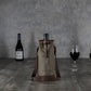 Beige waxed canvas wine tote with brown leather trim and adjustable shoulder straps, displayed with wine bottles and glasses