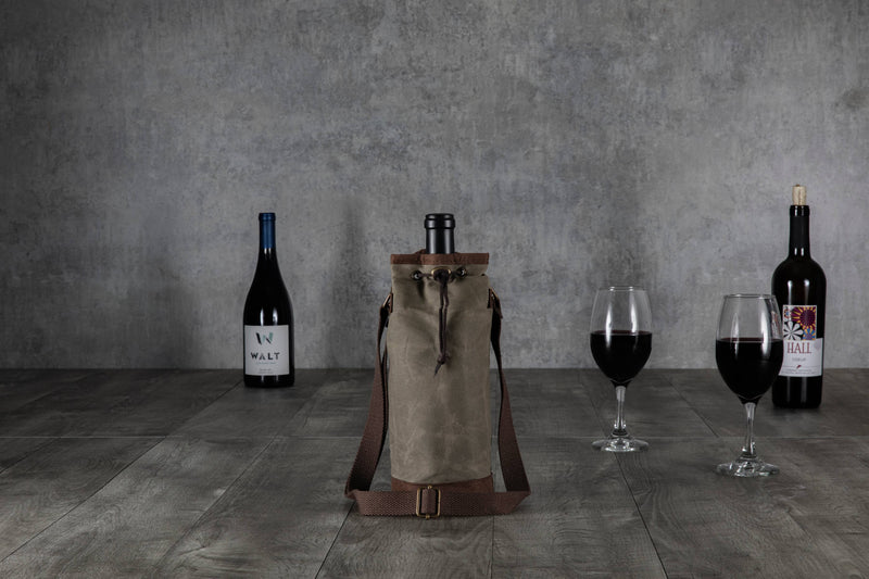 Beige waxed canvas wine tote with brown leather trim and adjustable shoulder straps, displayed with wine bottles and glasses