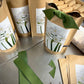 Kraft paper bags labeled with white paperwhite flowers and green stems, arranged with bulbs and planting materials in kraft packaging, displayed with green ribbon.