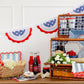 Patriotic 4th of July tableware display featuring Hamptons petite floral paper plates with blue florals, striped napkins, and star-spangled bunting.