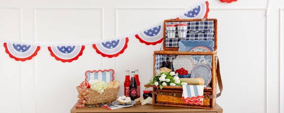 Patriotic 4th of July tableware display featuring Hamptons petite floral paper plates with blue florals, striped napkins, and star-spangled bunting.