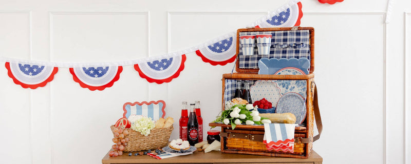 Patriotic 4th of July tableware display featuring Hamptons petite floral paper plates with blue florals, striped napkins, and star-spangled bunting.