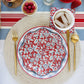 Red and white Floral Wave paper plate with botanical print, styled flatlay with gold cutlery, striped napkins, fresh berries, and drinks on marble surface.