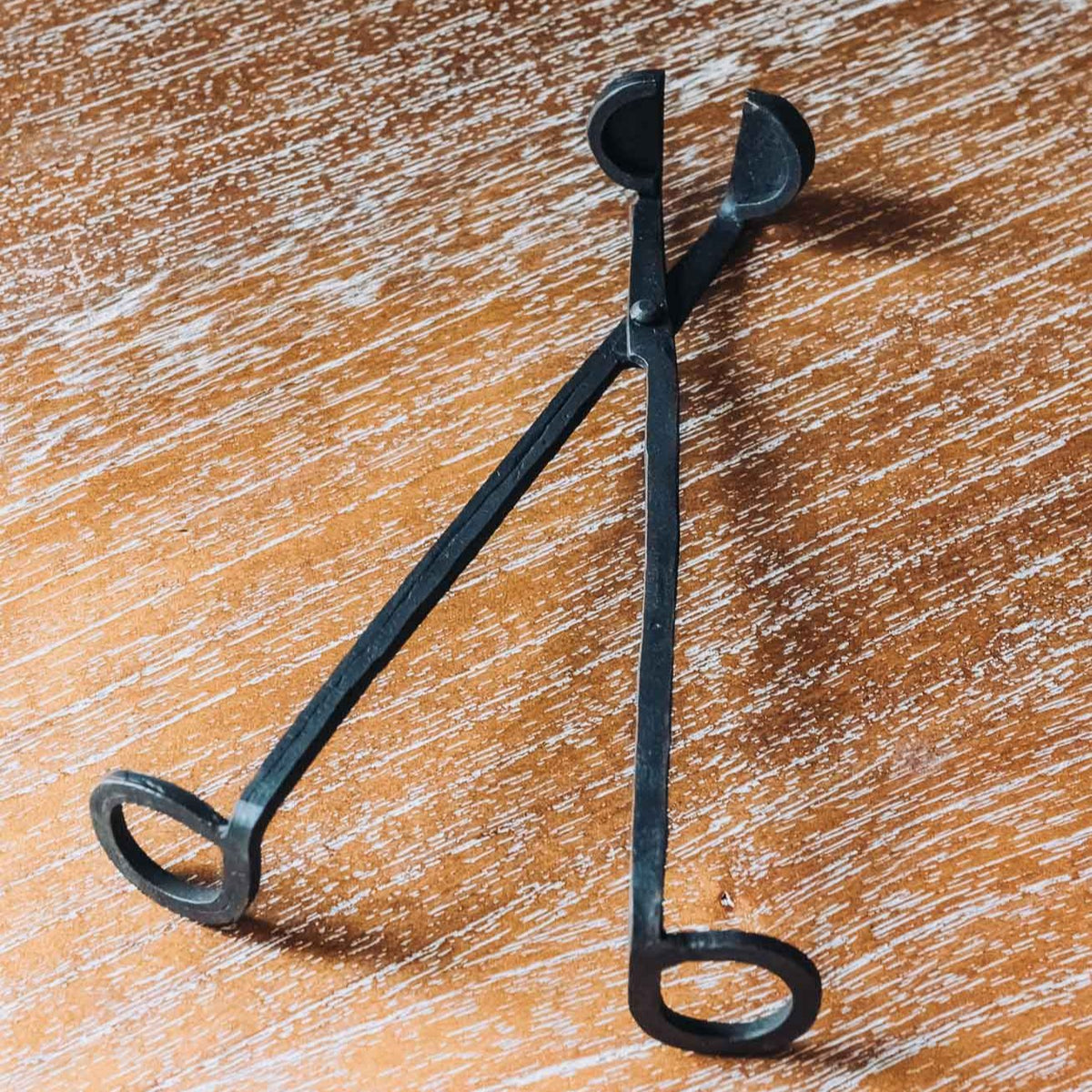 Black metal wick trimmer with dual handles on wood surface