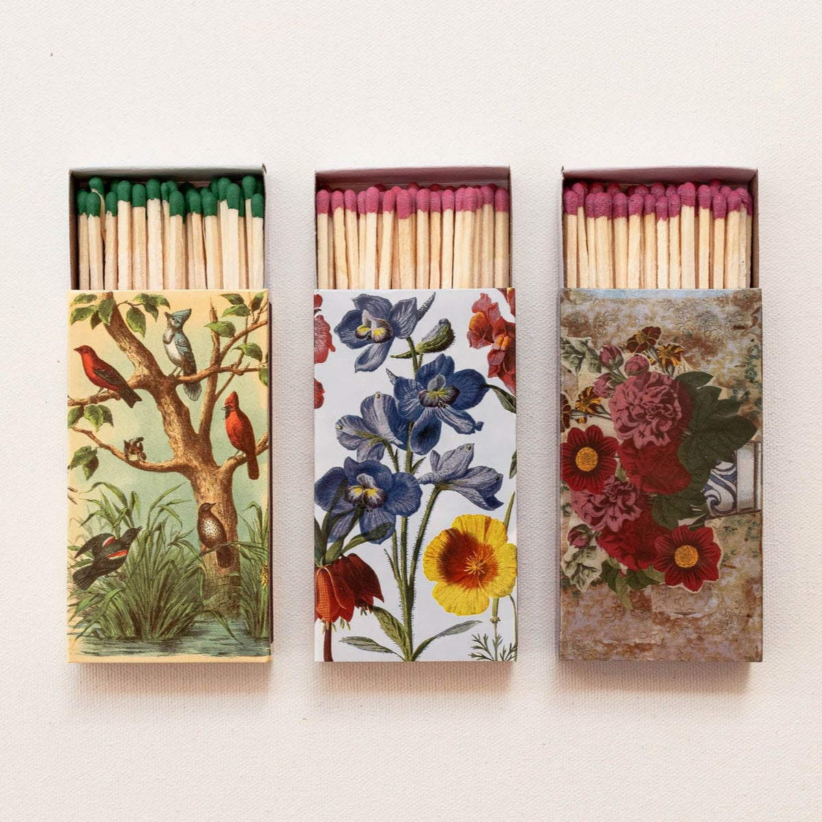 Three wooden match boxes with coordinating colored tips and vintage botanical bird and floral designs in green, cream, and burgundy tones.