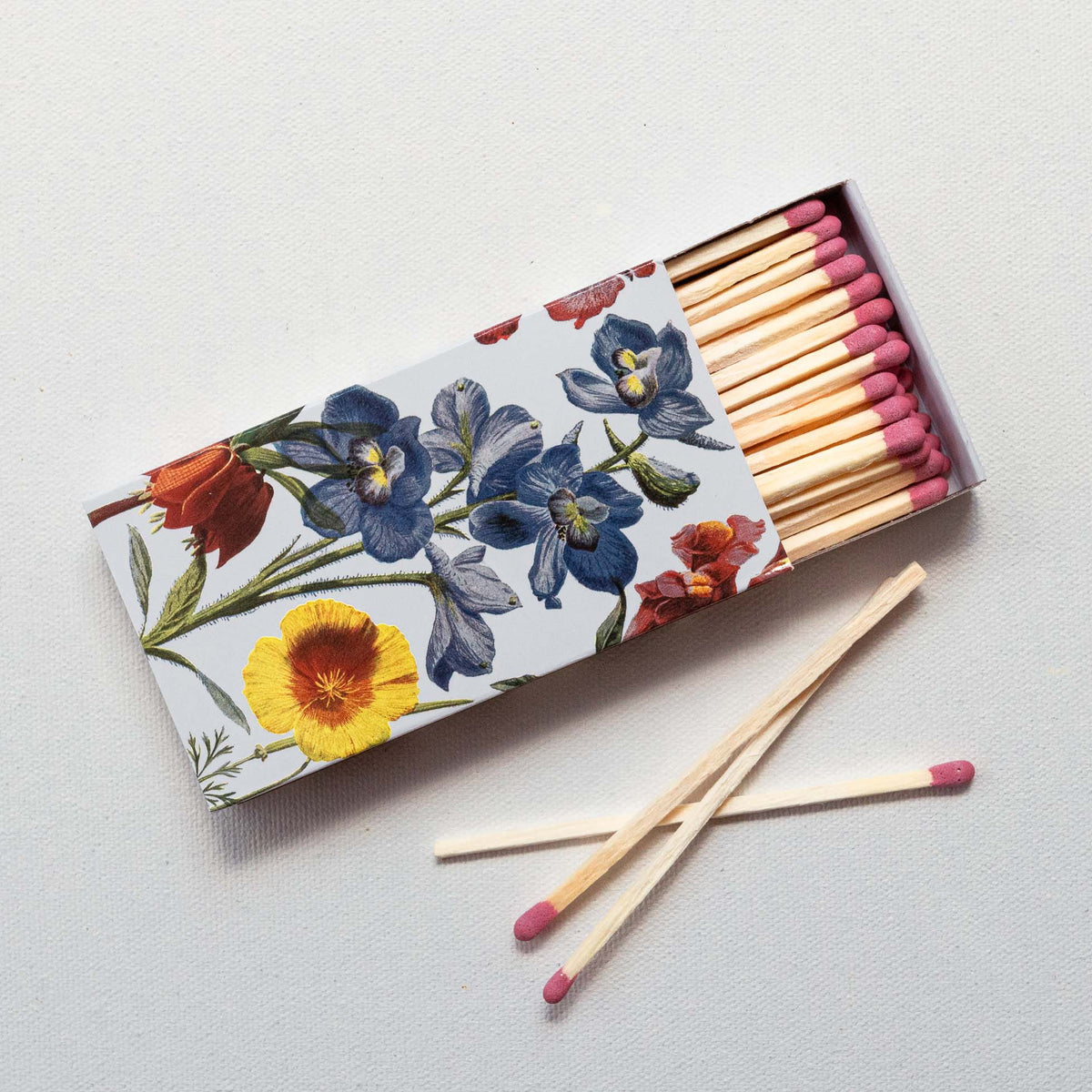 Wooden matchbox with floral design featuring blue, red, and yellow flowers; matches with pink tips visible inside open box and displayed in front.