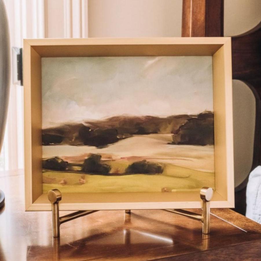 Wood-framed landscape artwork mounted on gold-tone metal easel with wooden base and cross-brace support