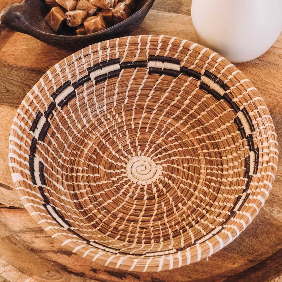 Handwoven round Bernarda Basket in natural tan with dark brown handle accents and radiating needle-weave pattern