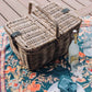 Natural rattan picnic basket with faux leather strap on patterned picnic blanket