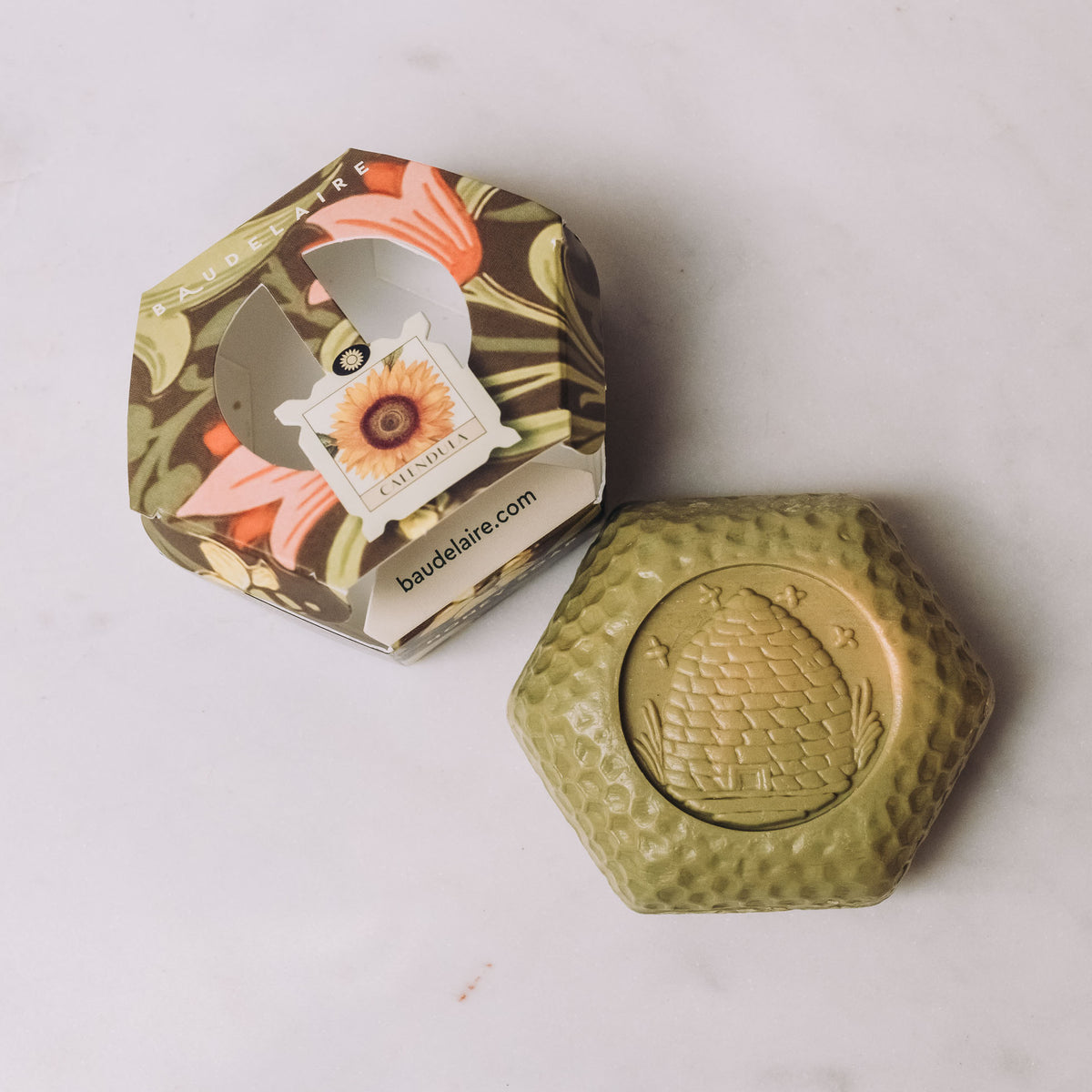 Honey soap in gold hexagonal box with botanical artwork and honeycomb-textured soap bar with embossed bee medallion
