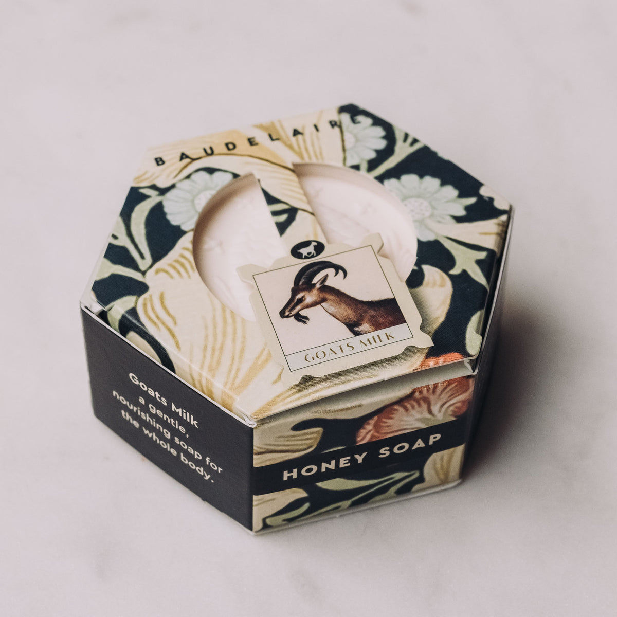 Hexagonal gift box with black and cream botanical design containing a large cream bar of Honey Soap by Baudelaire.