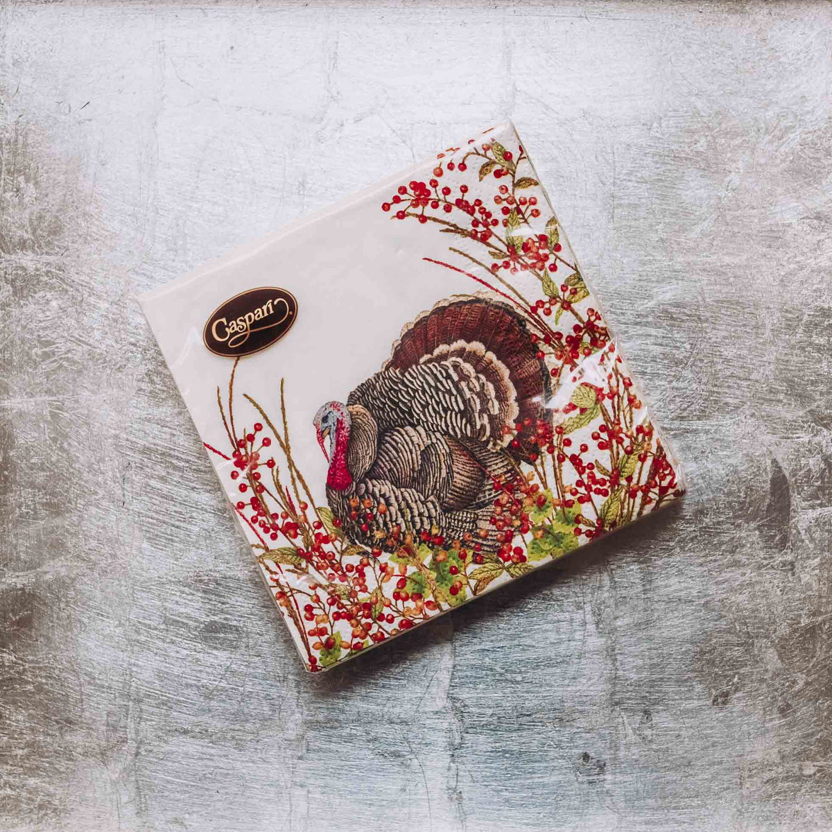 Caspari triple-ply cocktail napkins with illustrated turkey, red berries, and botanical border on cream background