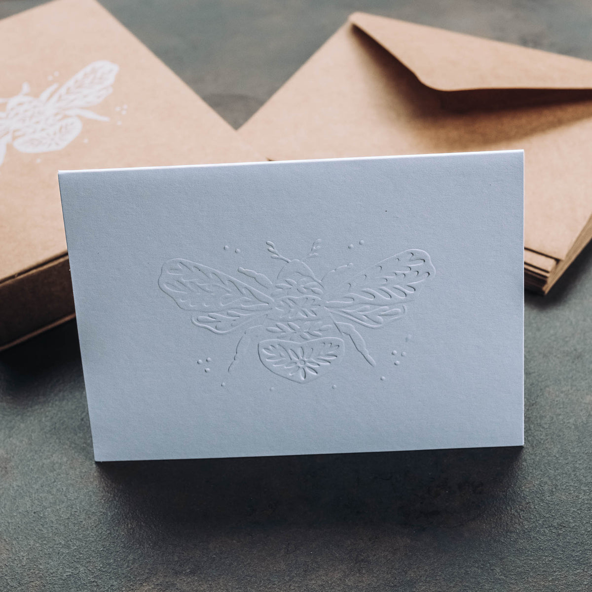 Light blue notecard with embossed bumble bee illustration featuring detailed wing patterns and decorative dots