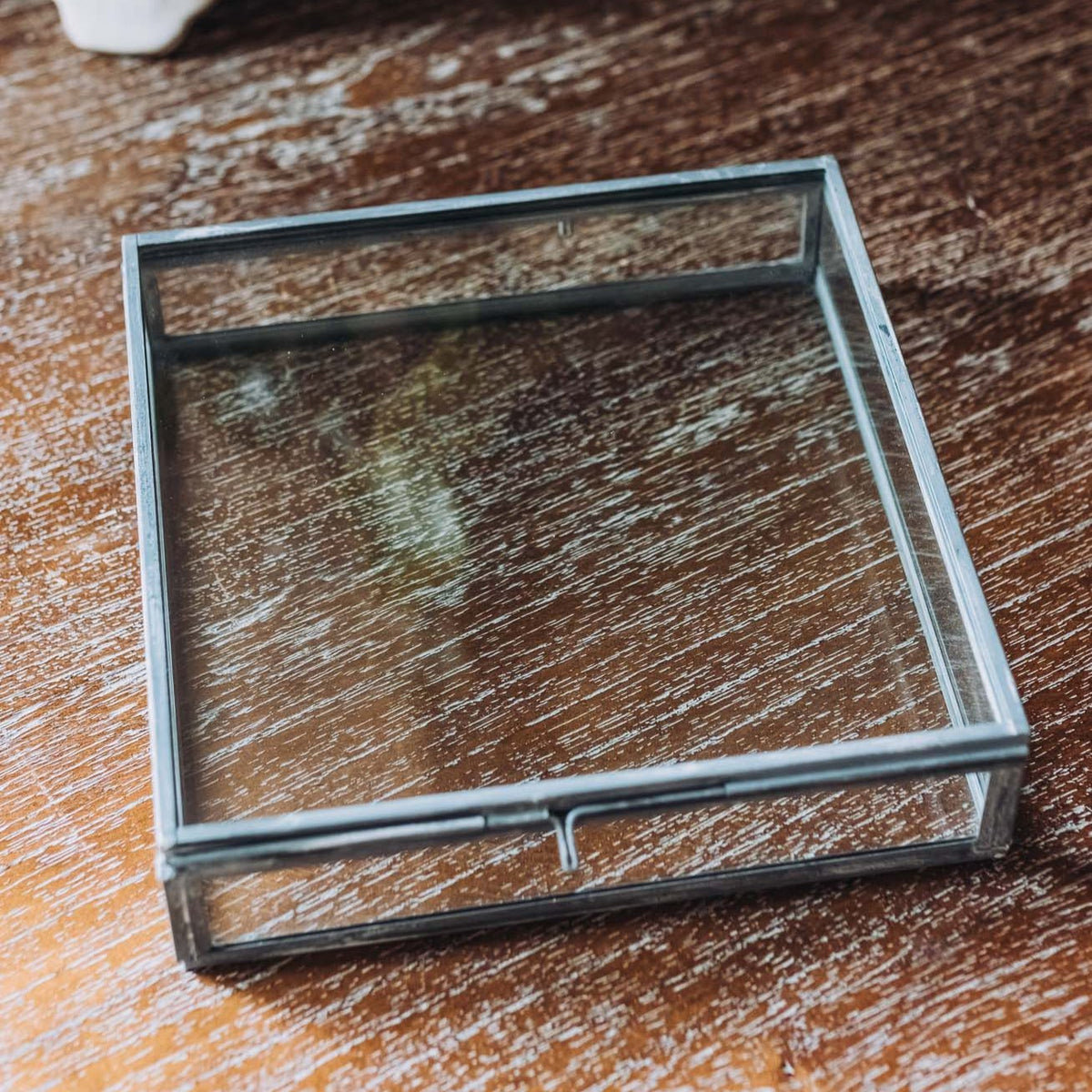 Clear glass memory box with square silver metal frame and glass lid, displayed on a distressed wood surface