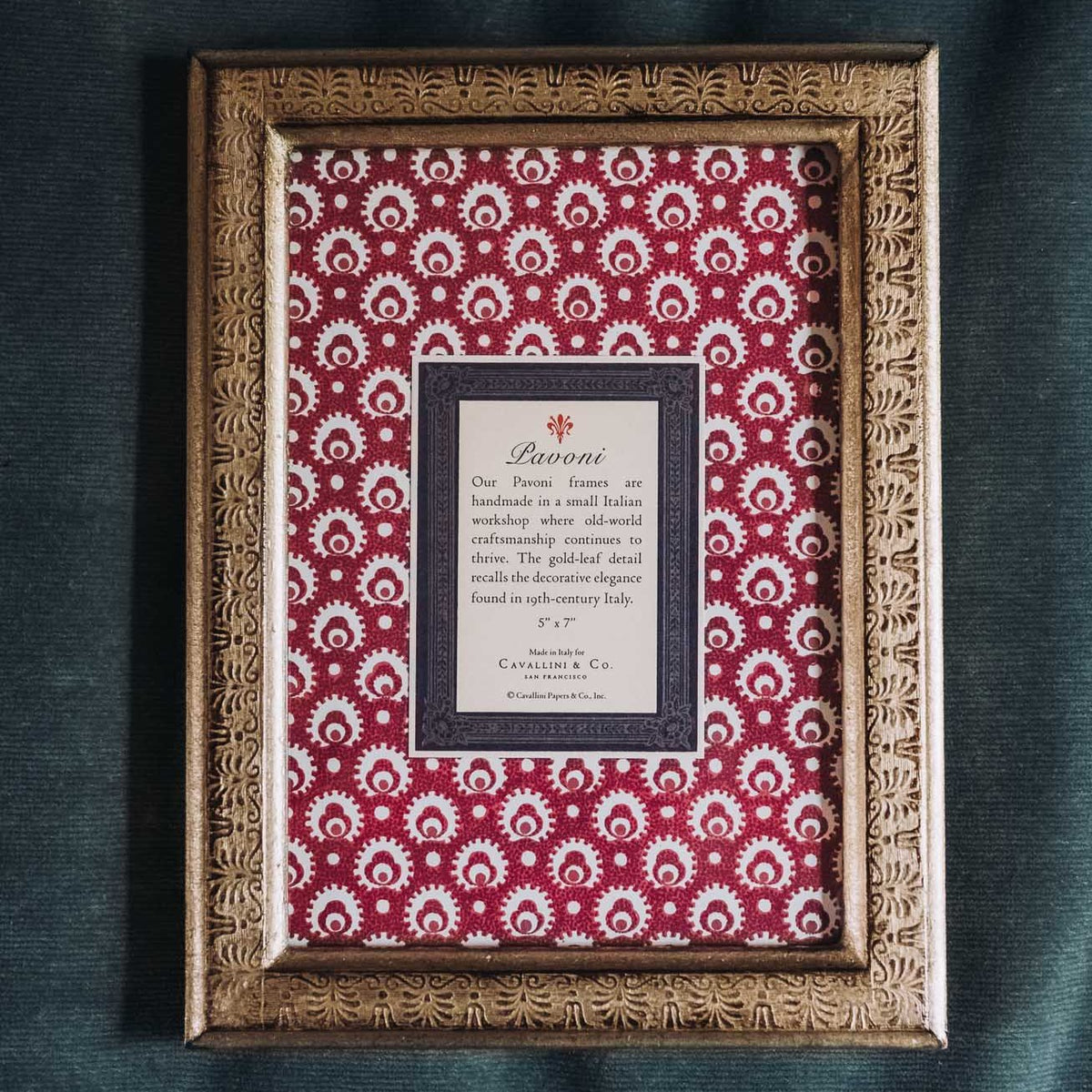 Rectangular wooden frame with ornate gold-leaf border surrounding burgundy and cream damask patterned matting with white text label centered inside.