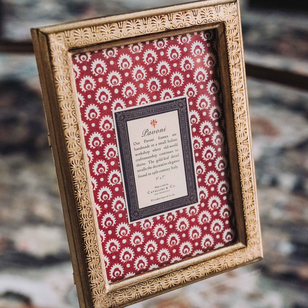 Gold leaf wooden frame with burgundy floral patterned mat and cream text card center, displayed at angle on gray surface