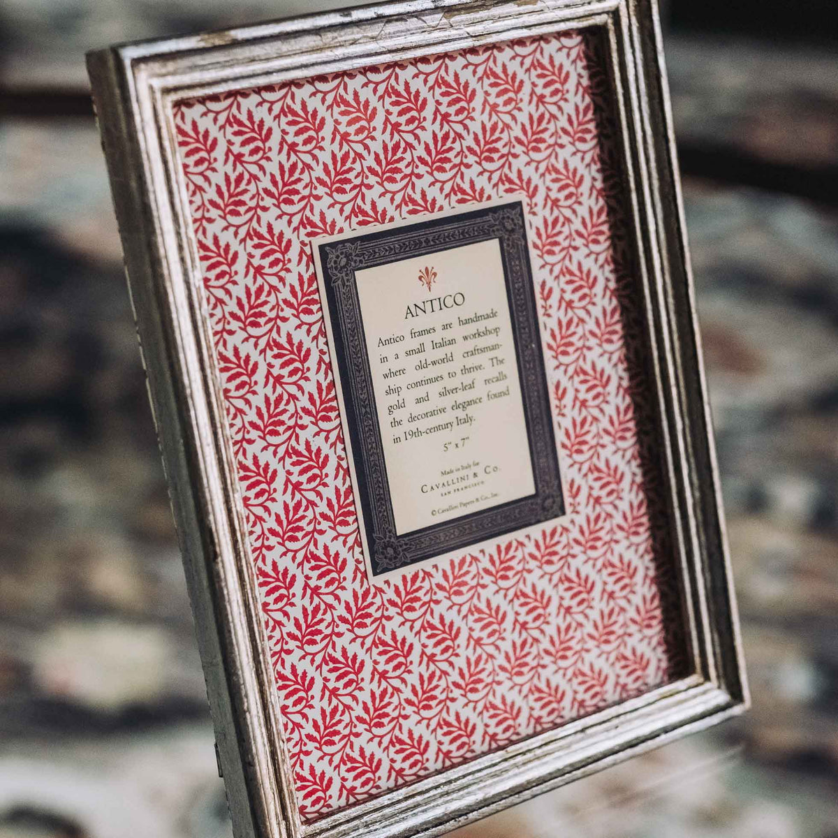 Silver-leaf wooden frame with ornamental edge holding cream label on red botanical patterned backing