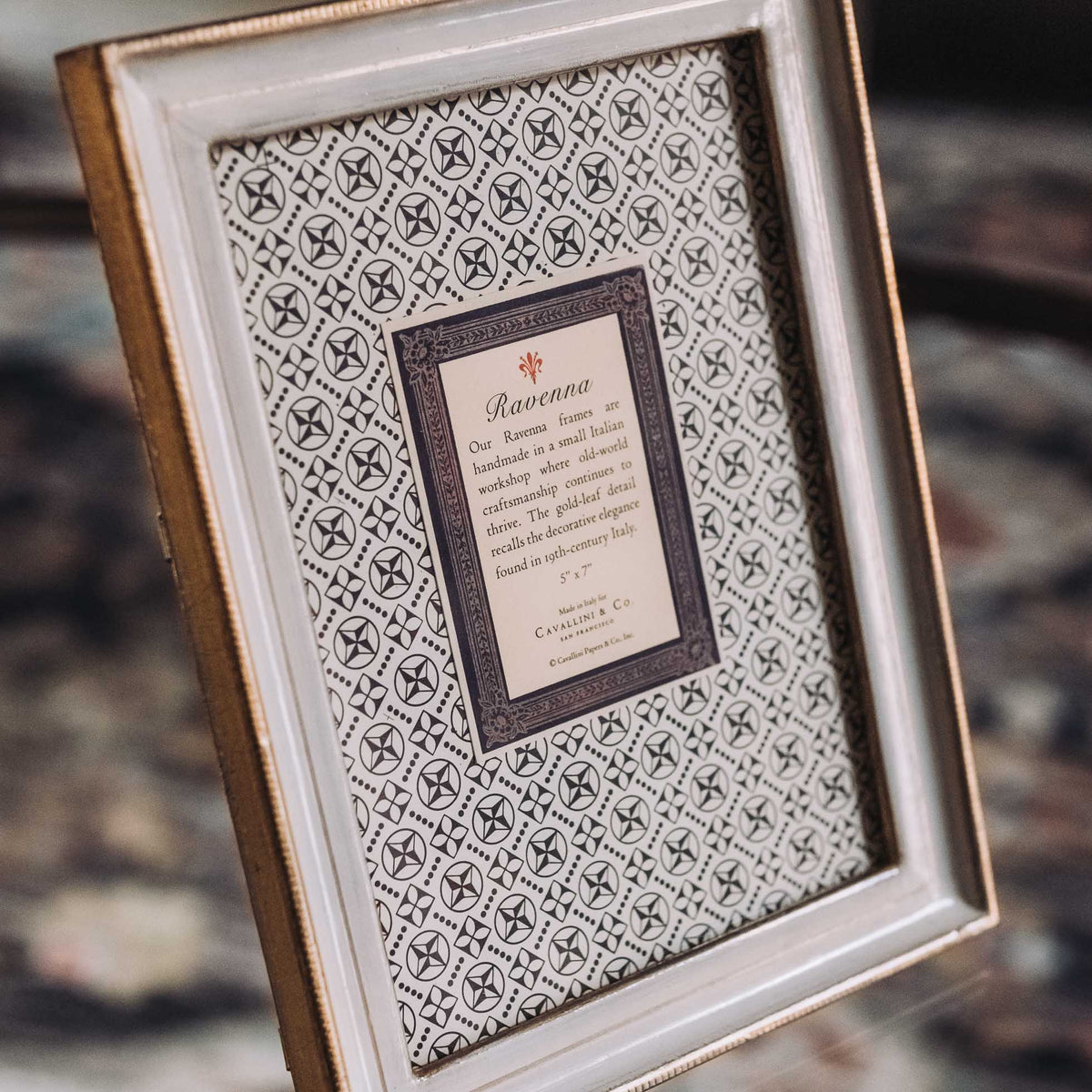 Cream wooden tabletop frame with gold leaf trim displaying italic text artwork on decorative paper background
