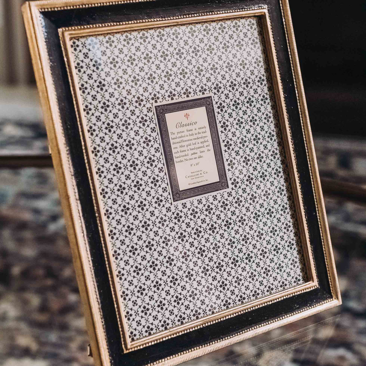 Black wooden picture frame with gold leaf trim and white patterned mat featuring geometric design and centered nameplate
