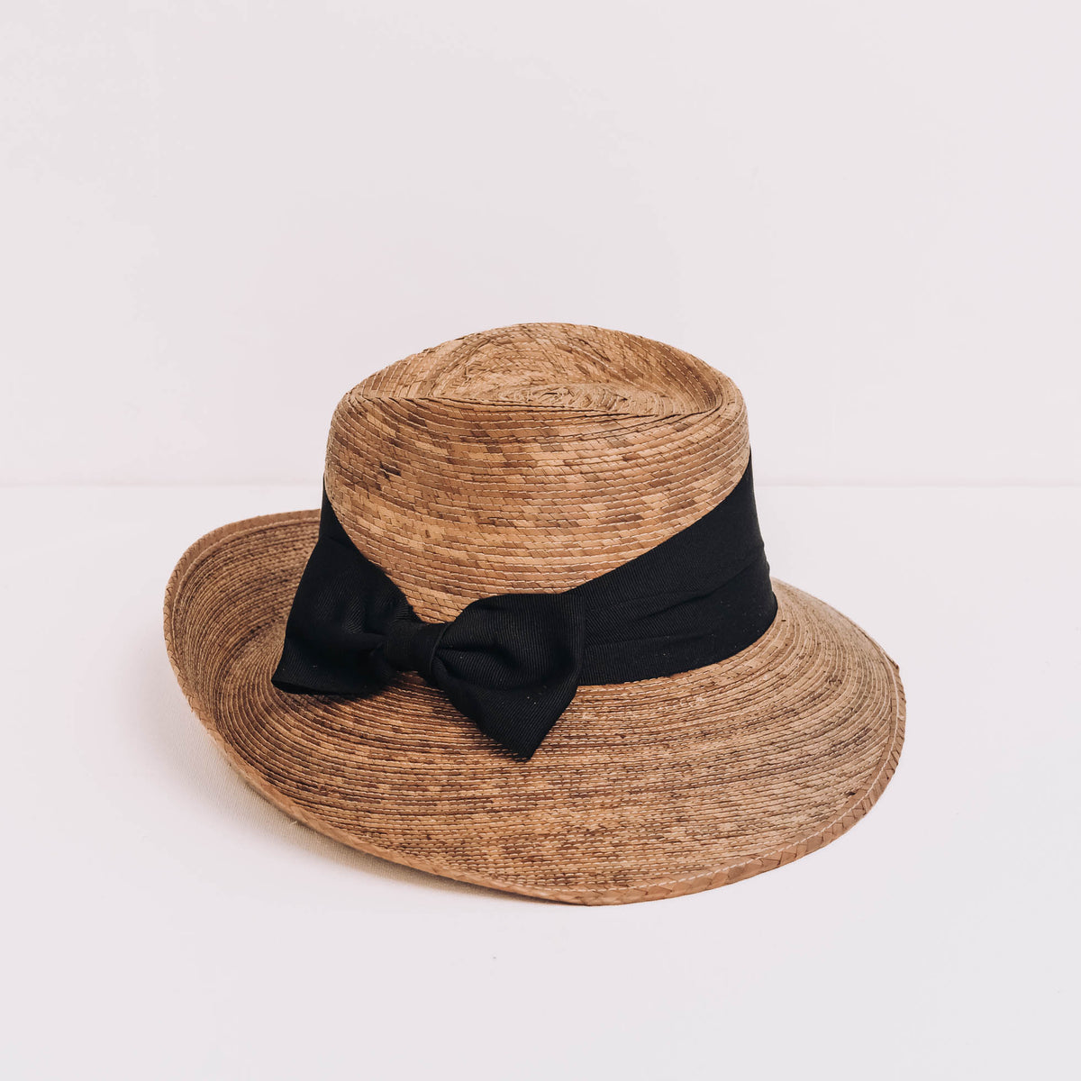 Handwoven palm straw hat with asymmetrical brim and black ribbon bow, natural tan color, UPF 50+ sun protection