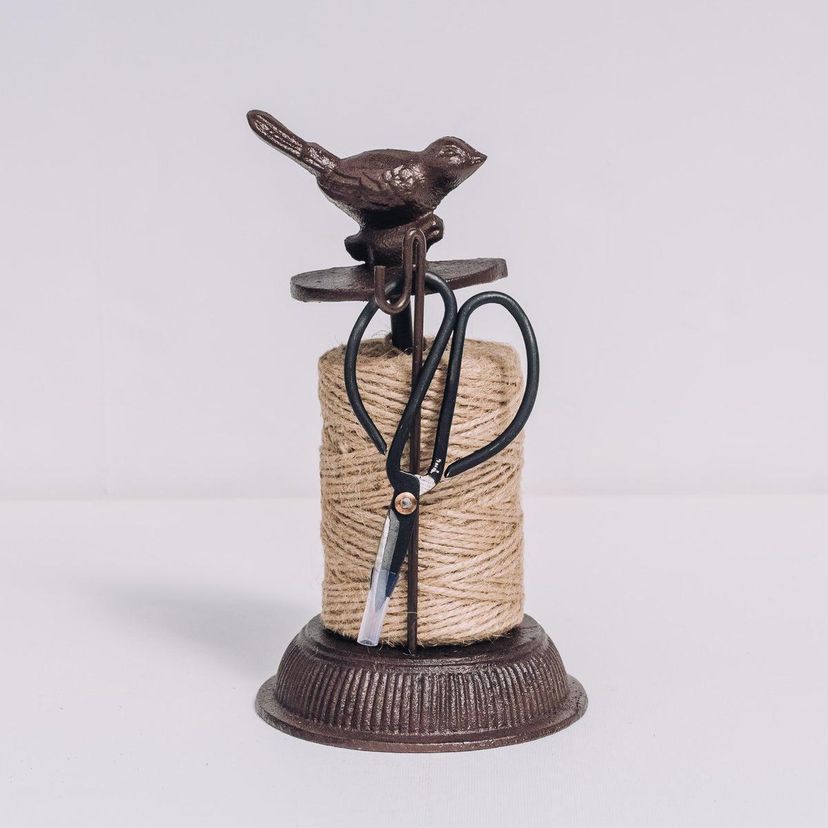 Cast iron garden twine dispenser with bird-shaped topper, jute twine, and integrated black scissors on pedestal base.