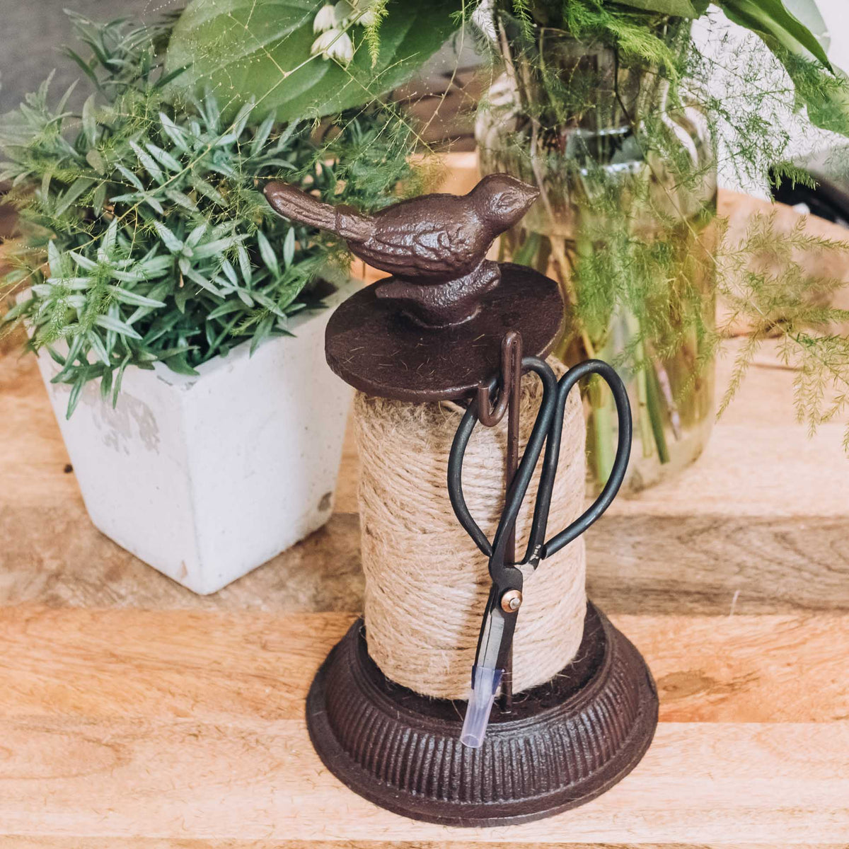 Cast iron garden twine dispenser in antique brown with jute twine, decorative birds, and looped scissors on wooden surface.