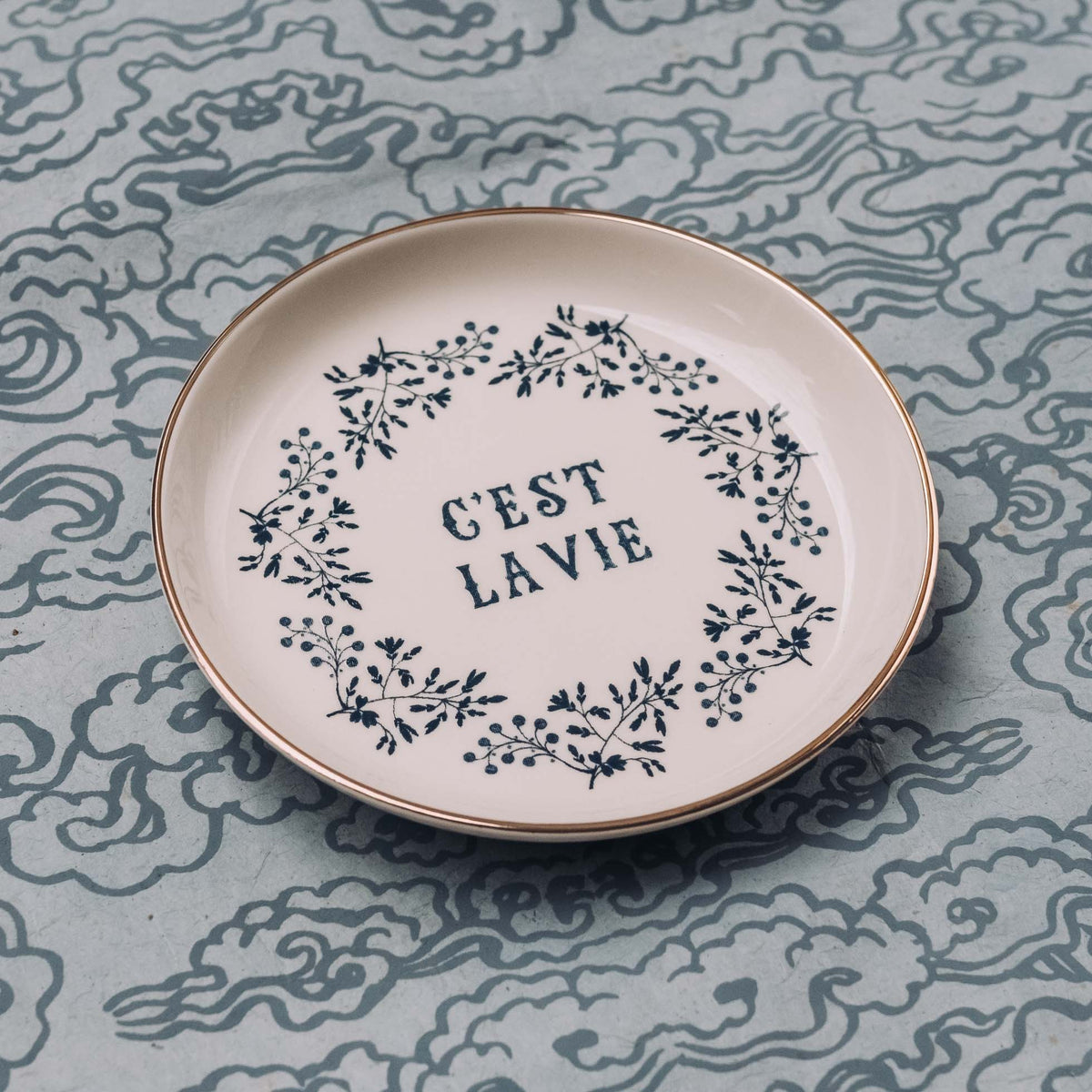 White ceramic trinket dish with "C'est La Vie" text and leaf wreath design in navy blue