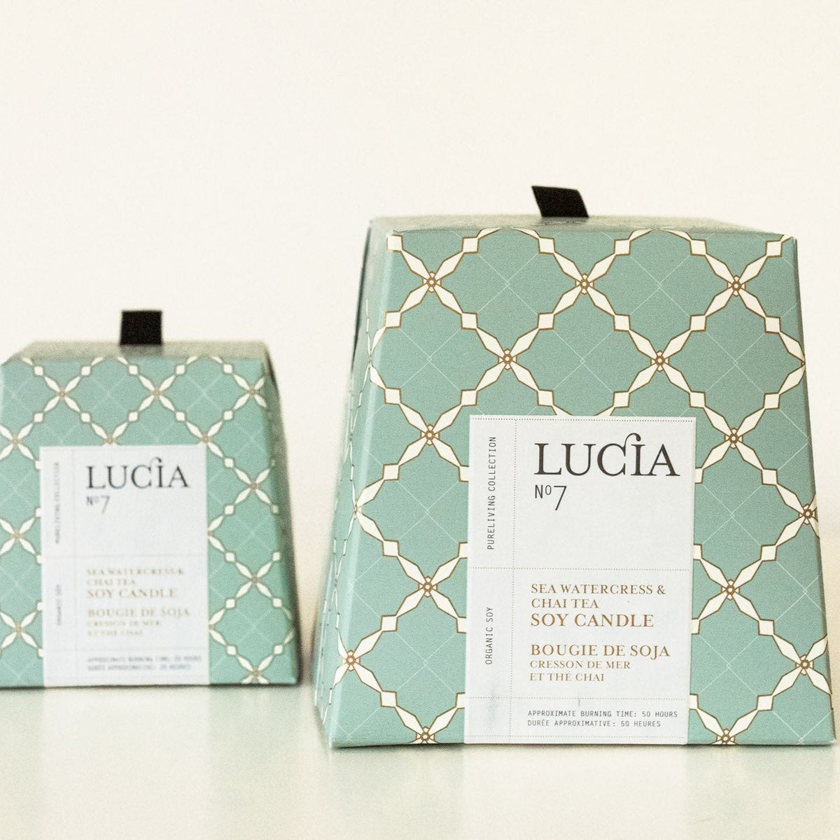 Two sage-green soy candle boxes with cream trellis pattern: smaller votive and larger jar, both labeled Lucia No.7 Sea Watercress & Chai Tea.