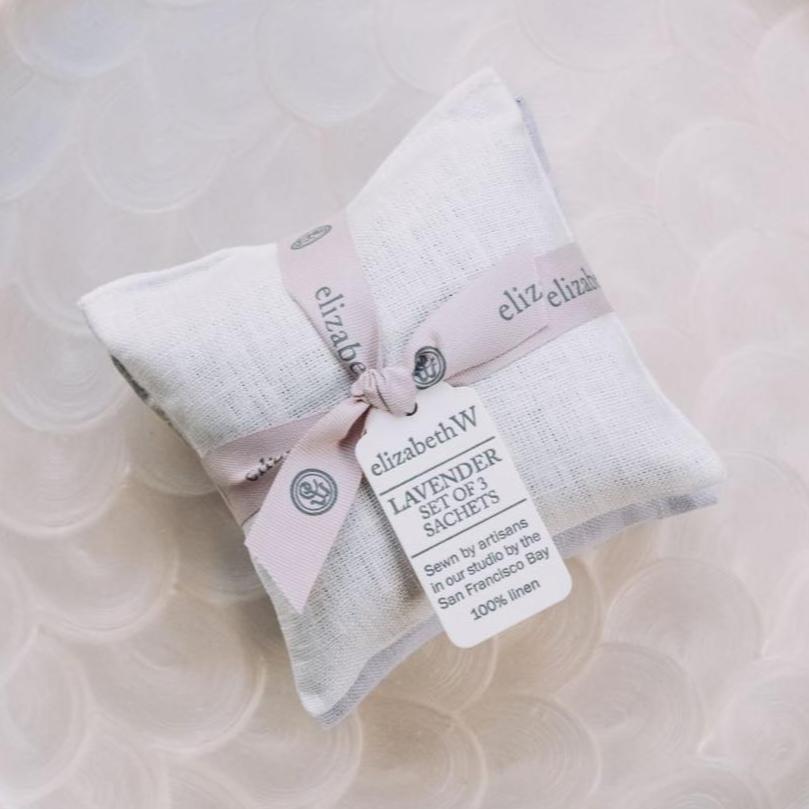 Three white linen lavender sachets tied with pale pink ribbon bow, elizabethW branding visible on attached label
