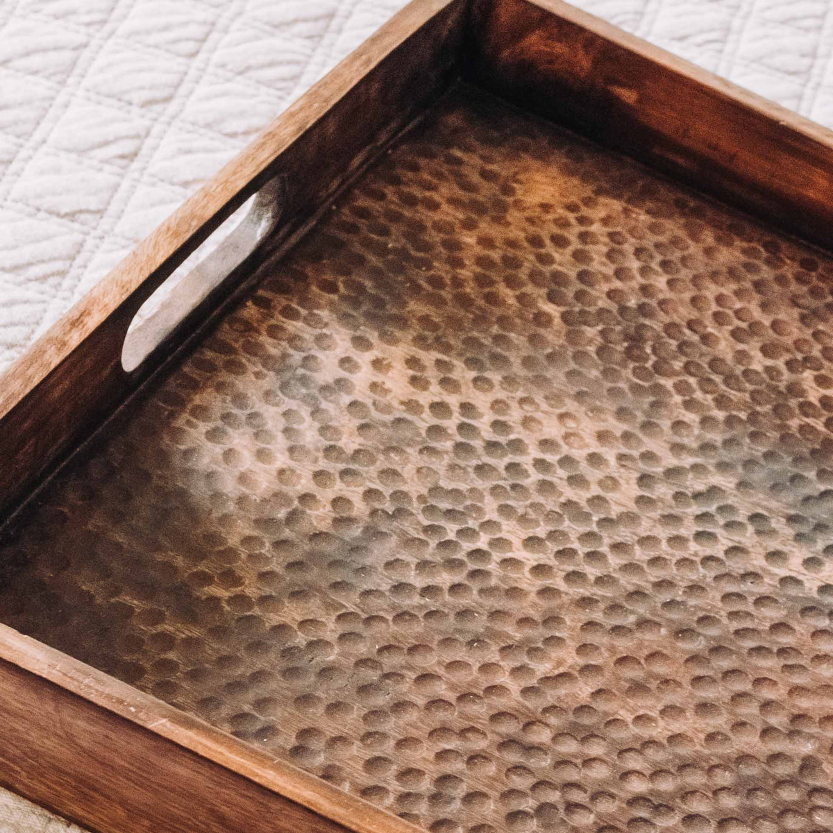 Brown wooden serving tray with hammered finish and white inset handles, showing dimpled texture surface