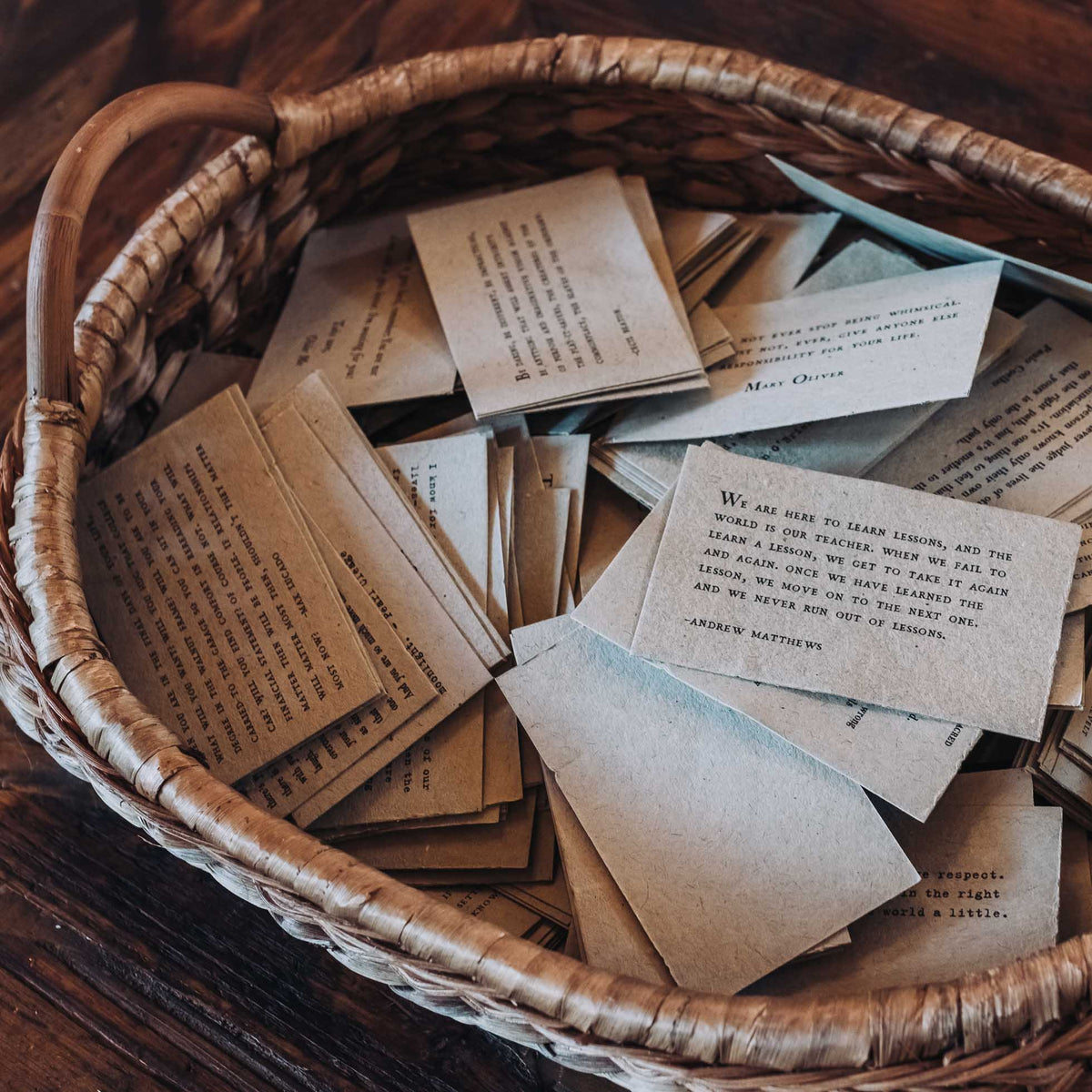 Assorted handcrafted note cards in cream and light blue scattered in a woven basket, featuring typewritten Christmas quotes and inspirational text in vintage style