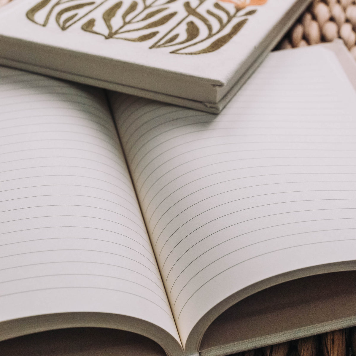 Cream hardcover journal open to show ruled lined pages, with gold embroidered floral stems on front cover.