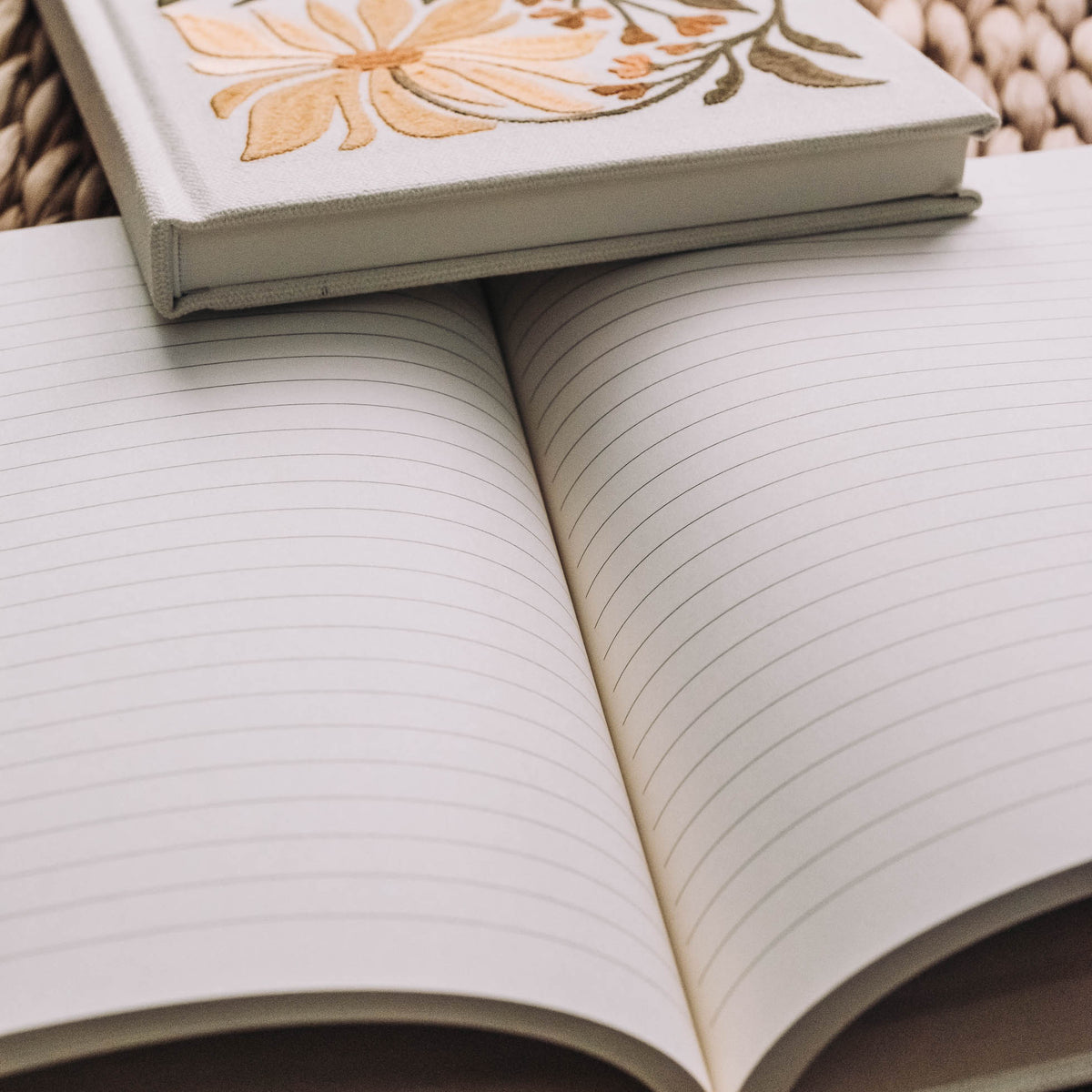 Cream hardcover journal with embroidered lily and green stems on cover, open to reveal lined blank pages