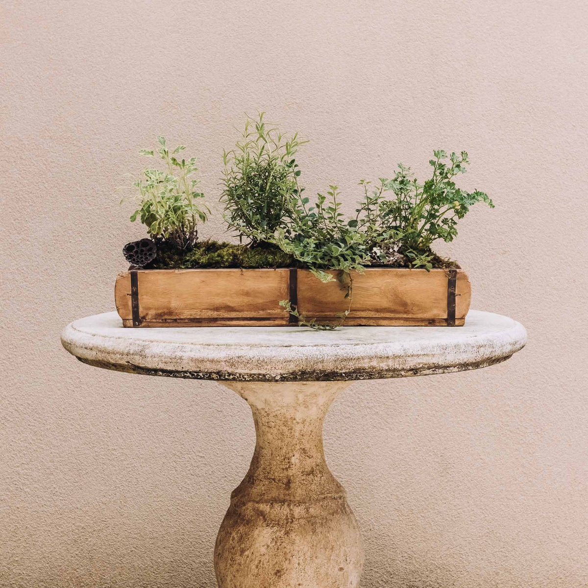 Terracotta-brown wooden double brick mold planter holding green herbs on a stone pedestal table