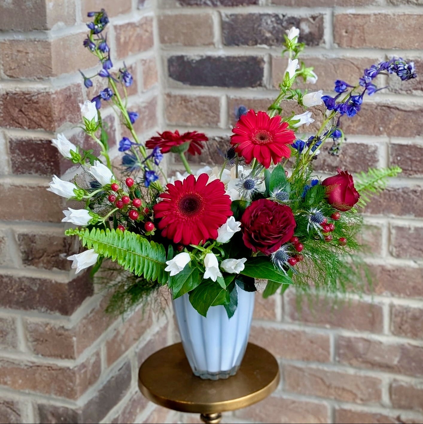 Floral arrangement with red and white flowers in a blue vase against a brick wall.