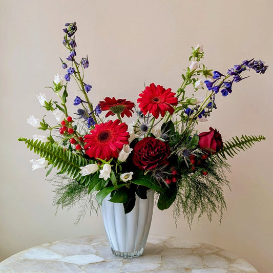 Bouquet of red, white, and purple flowers in a white vase on a marble surface with a beige wall background.
