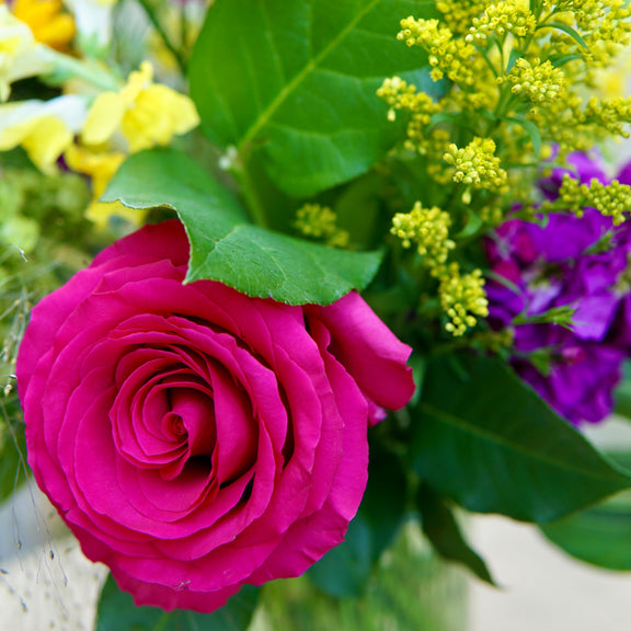 Bouquet of flowers including a pink rose, yellow sunflower, and green leaves.