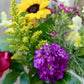 Bouquet of flowers with yellow sunflower, purple flower, and green leaves.