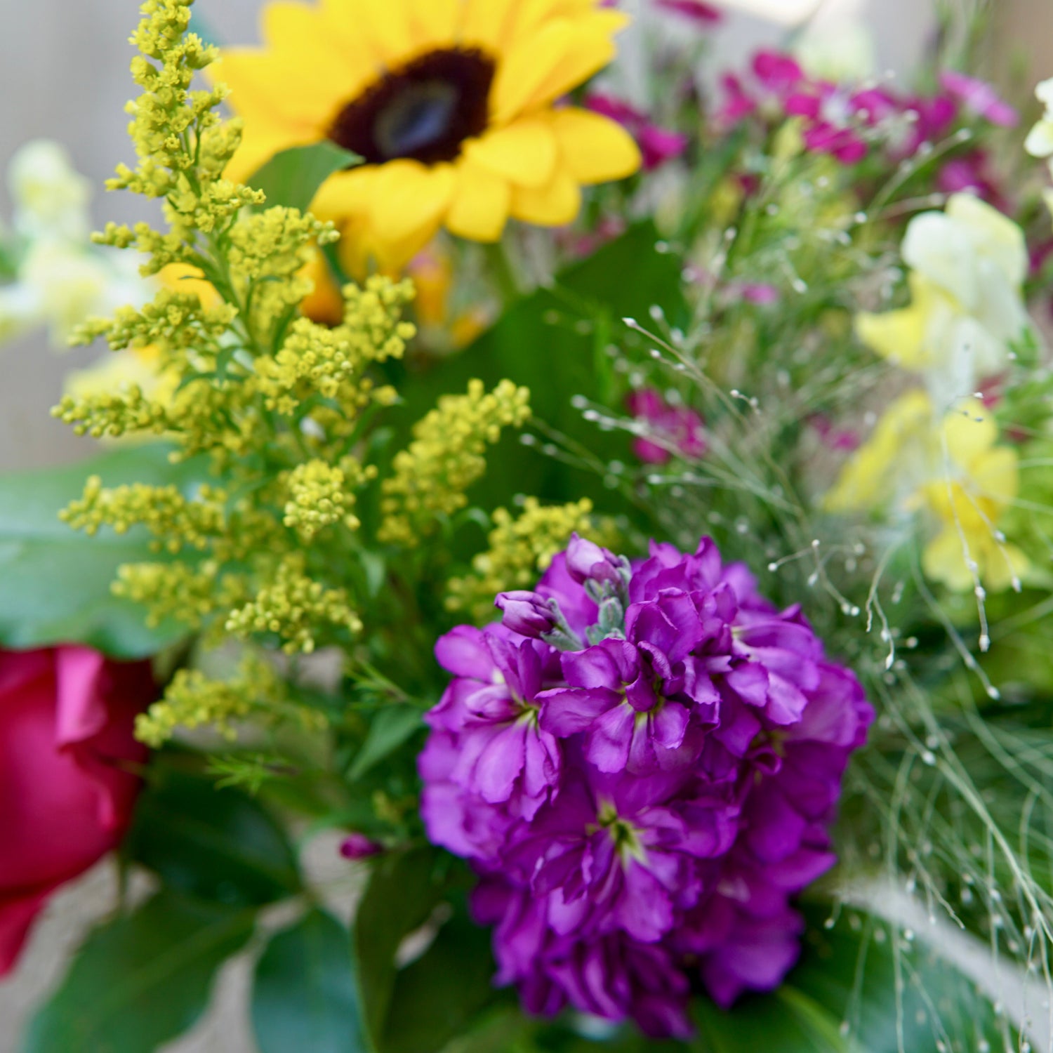 Bouquet of flowers with yellow sunflower, purple flower, and green leaves.