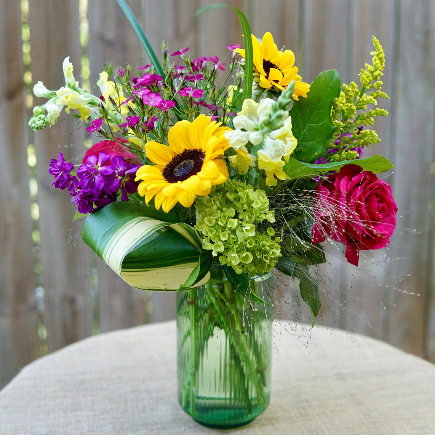 Bouquet of flowers in a green vase on a textured surface with a blurred background