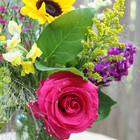 Bouquet of flowers including a pink rose and sunflower with blurred background