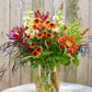 Bouquet of flowers in a clear vase on a white surface with a wooden background