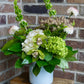Floral arrangement in a white pot on a wooden stool against a brick wall